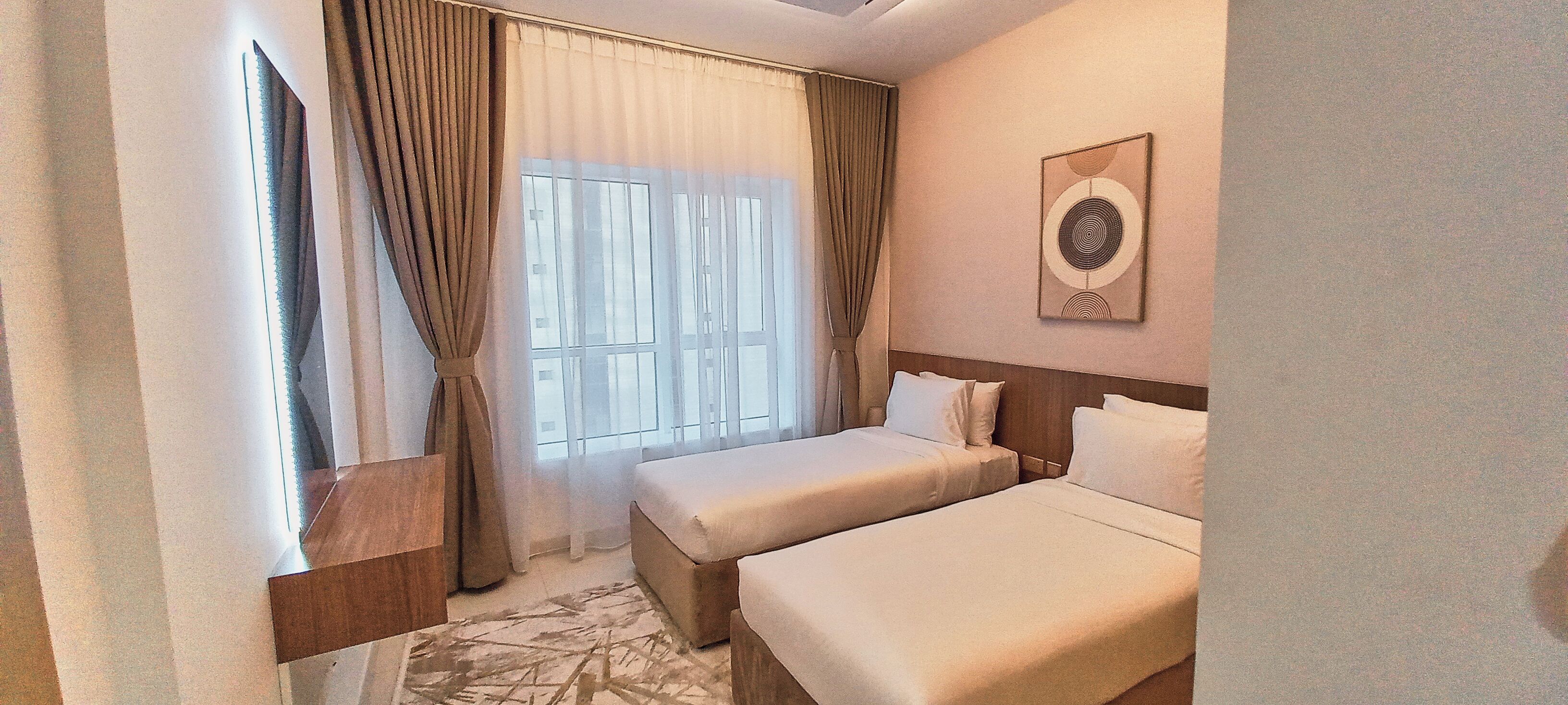 A hotel room with two beds, a large window with curtains, a wooden headboard, and a wall-mounted artwork.