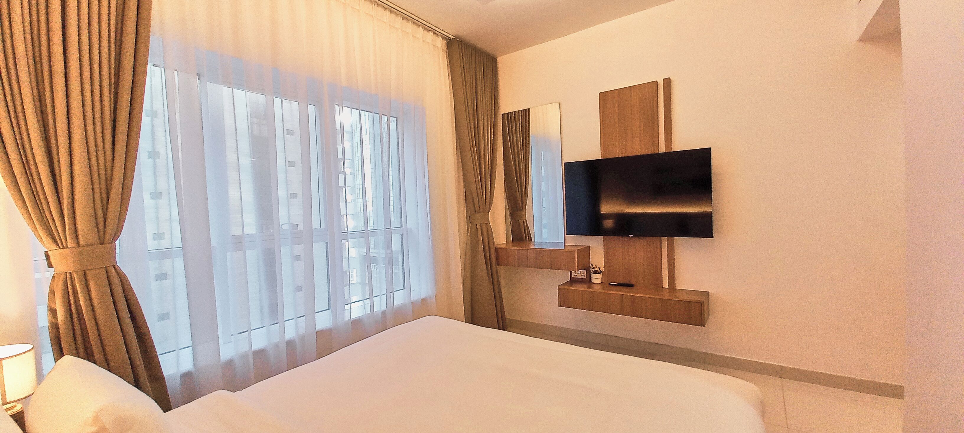 Habitación de hotel con una cama grande, un televisor montado en la pared y una ventana con cortinas.