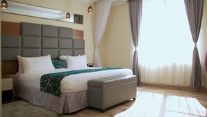Une chambre d’hôtel moderne avec un grand lit, une tête de lit grise et un petit coin salon.