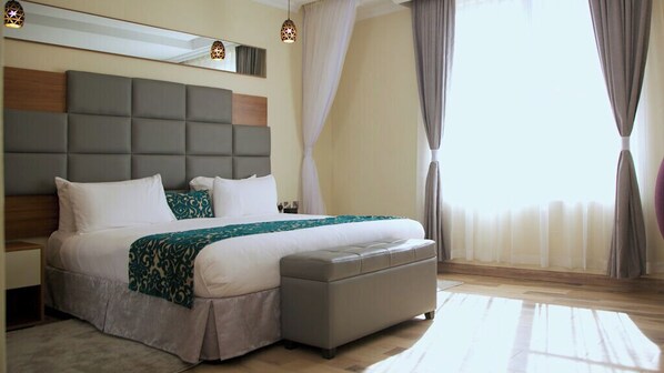 Une chambre d’hôtel moderne avec un grand lit, une tête de lit grise et un petit coin salon.