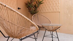A wicker chair and table set against a textured wall with a door and a plant. - Stay Passport Morocco Spa Incheon Songdo (Incheon)