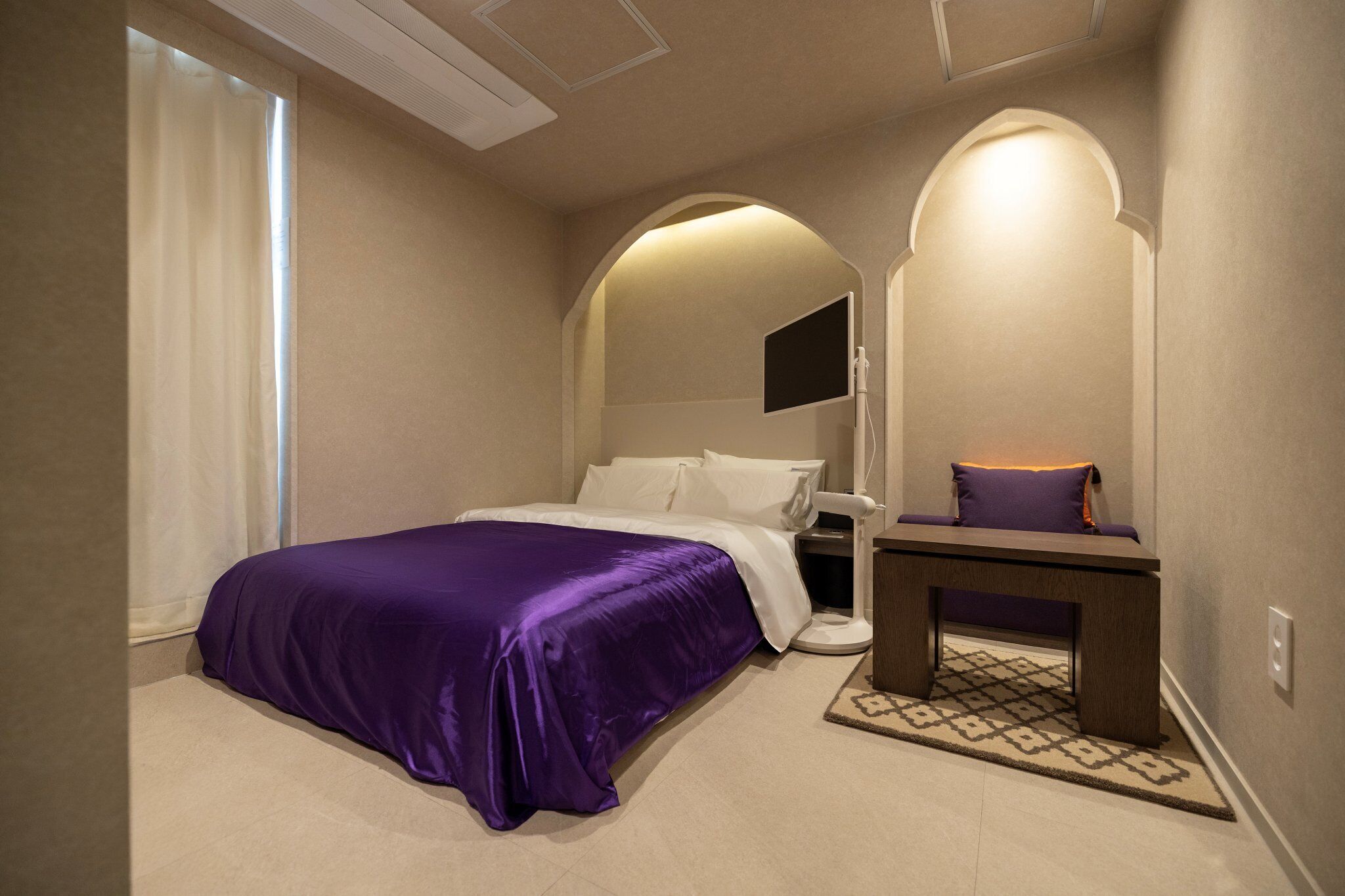 A bedroom with a bed, a bedside table, a mirror, and a window.
