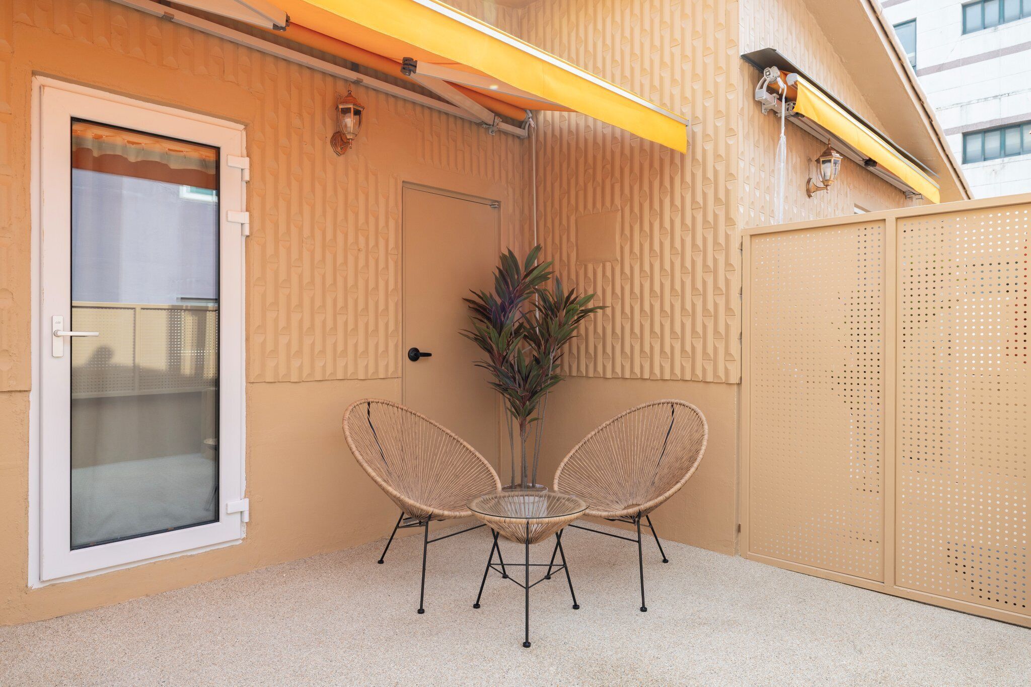A small outdoor seating area with two wicker chairs and a table, a door, and a yellow awning.