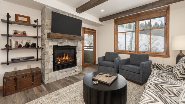 A cozy living room with a stone fireplace, two grey armchairs, a patterned sofa, and a round coffee table. - Two Bedroom Condos at Zephyr Mountain Lodge - Winter Park CO (Winter Park)