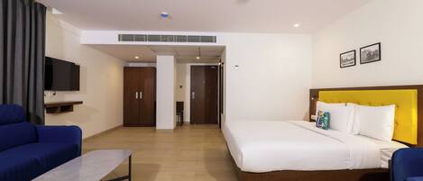 A hotel room with a bed, a sofa, a small table, a TV, and a ceiling fan.
