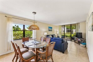 A modern living room with a glass dining table, wicker chairs, a blue sofa, and a TV.