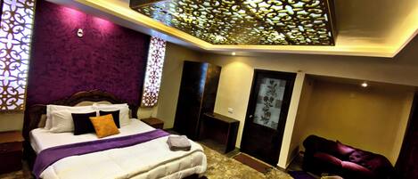 A modern bedroom with a large bed, a small sofa, and a decorative ceiling panel.