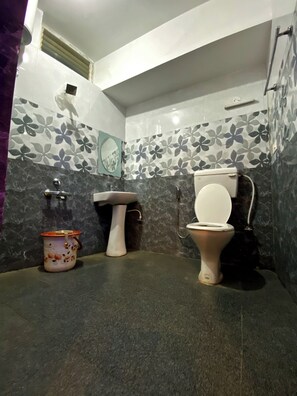 Une salle de bain avec des toilettes, un lavabo et un seau.