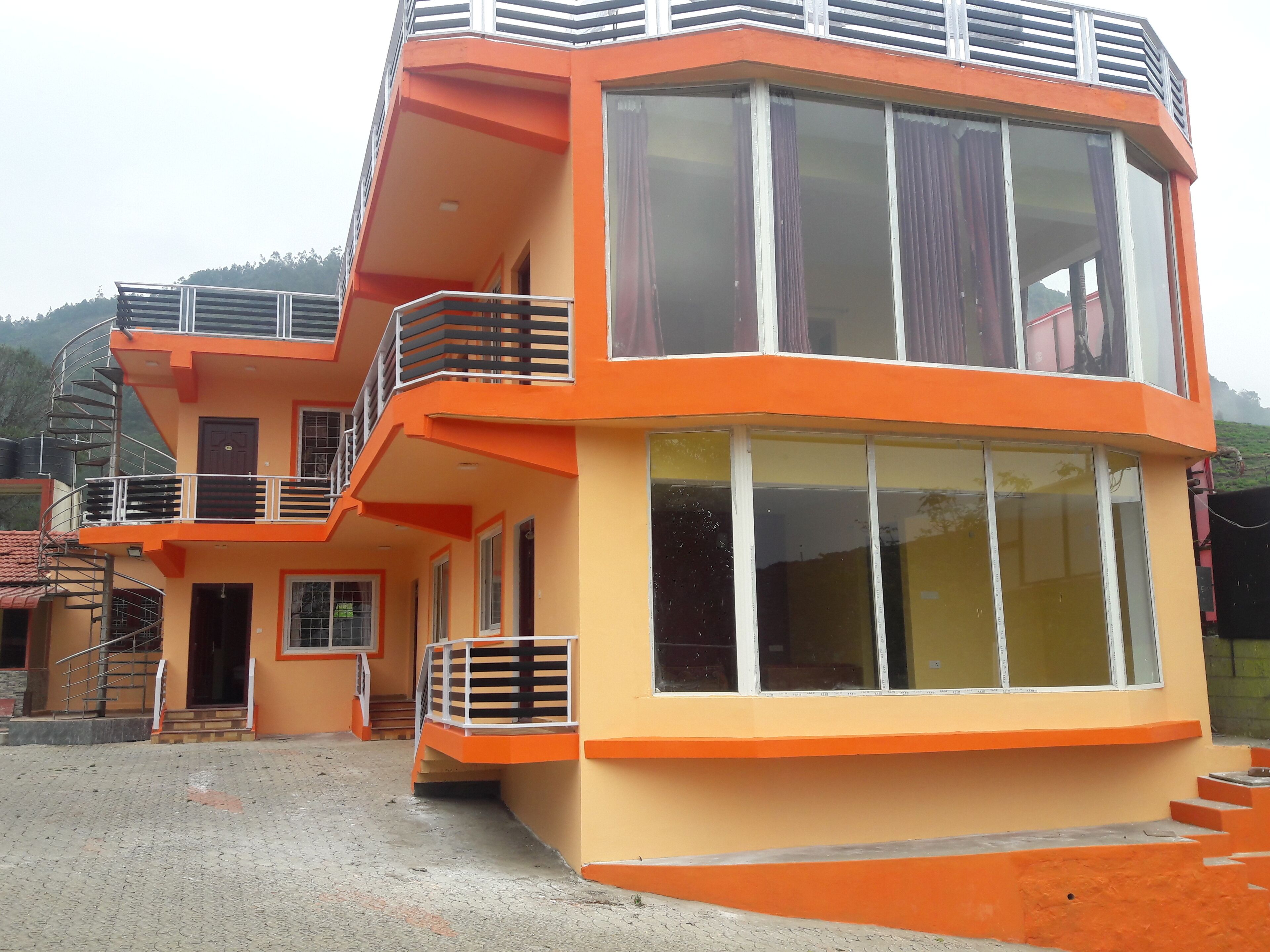 Un immeuble à plusieurs étages, aux façades extérieures de couleur orange et beige, doté de grandes fenêtres et d’un balcon avec une rambarde en métal.