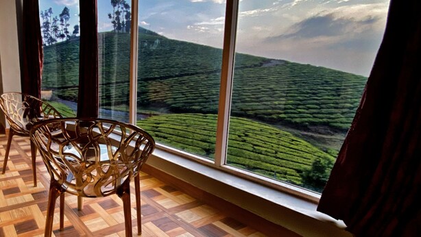 A room with large windows offering a view of a green landscape, a wooden parquet floor, and a chair. - Magic Mist Resort A Boutique Resort (Ooty)