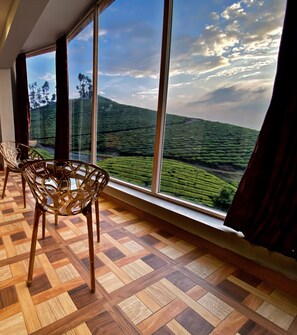 Une pièce dotée de grandes fenêtres donnant sur un paysage verdoyant, d’un parquet en bois et d’une chaise.