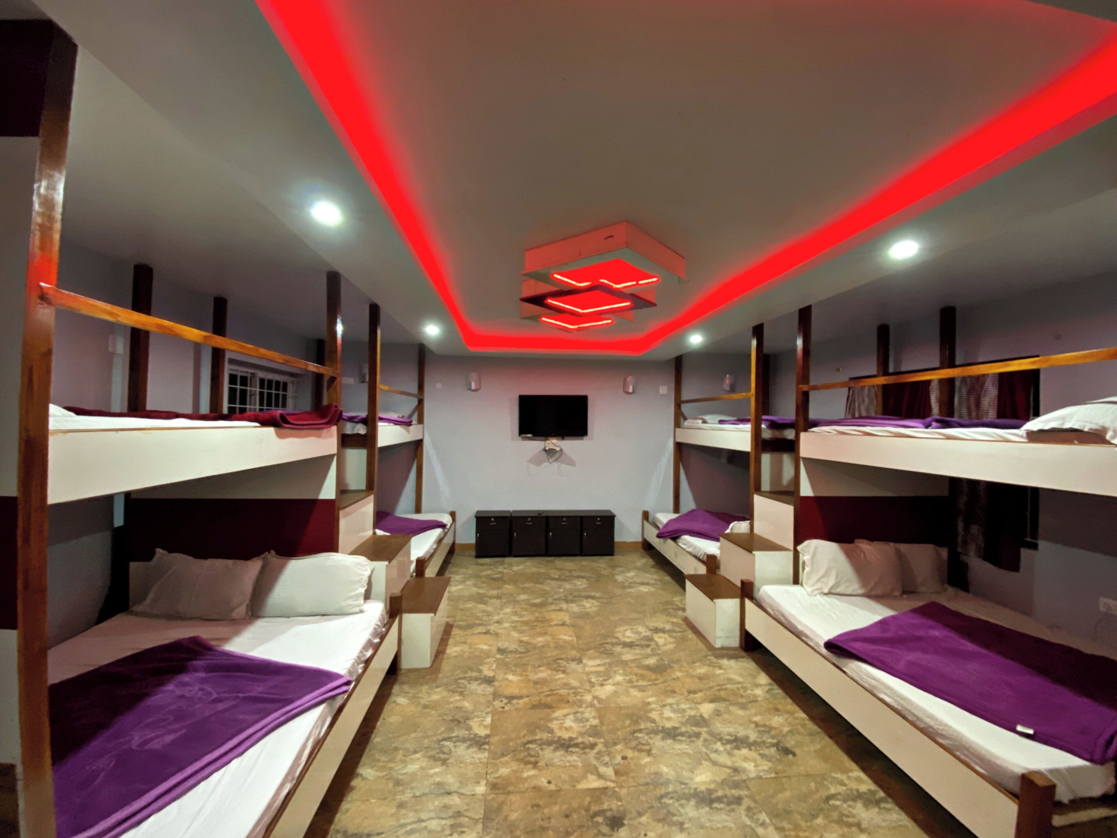 A dormitory room with bunk beds, a television, and a red neon light fixture.