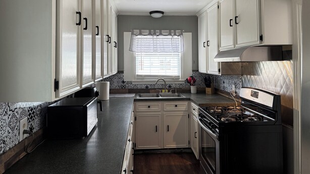 Una cocina con armarios blancos, estufa, fregadero y salpicadero con diseño.