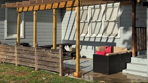 Un espacio de estar al aire libre techado, con una pérgola de madera, un sofá de mimbre y una mesita.