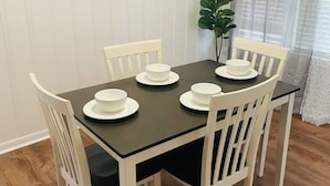 Una mesa de comedor con sillas blancas, dispuesta con platos y tazones blancos.