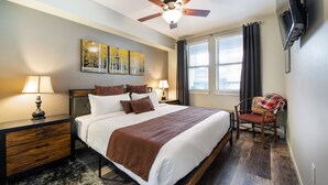 A bedroom with a bed, two bedside tables with lamps, a ceiling fan, a TV mounted on the wall, and a window with curtains. - Winter Park Resort Lodging - Convenient Condos (Winter Park)