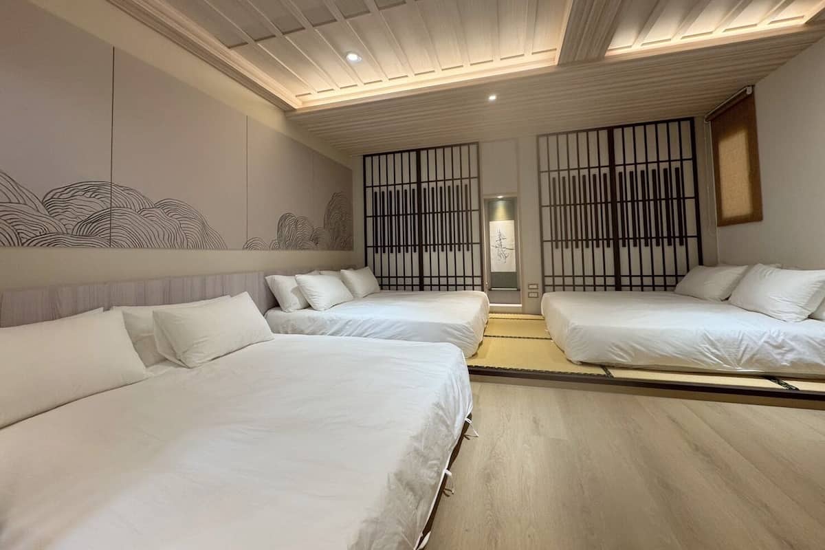 Une chambre d’hôtel moderne avec deux lits simples, un plancher en bois et un mur décoratif orné d’un motif ondulé.