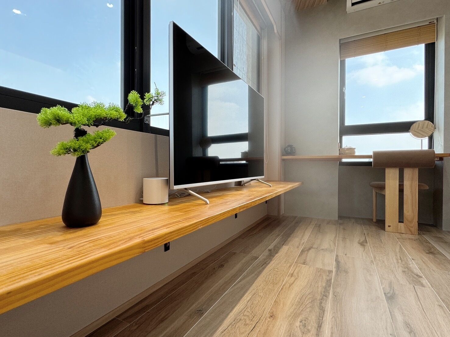 Una sala de estar moderna con un televisor de pantalla plana en un estante de madera, una pequeña planta en maceta y una silla de estilo minimalista.