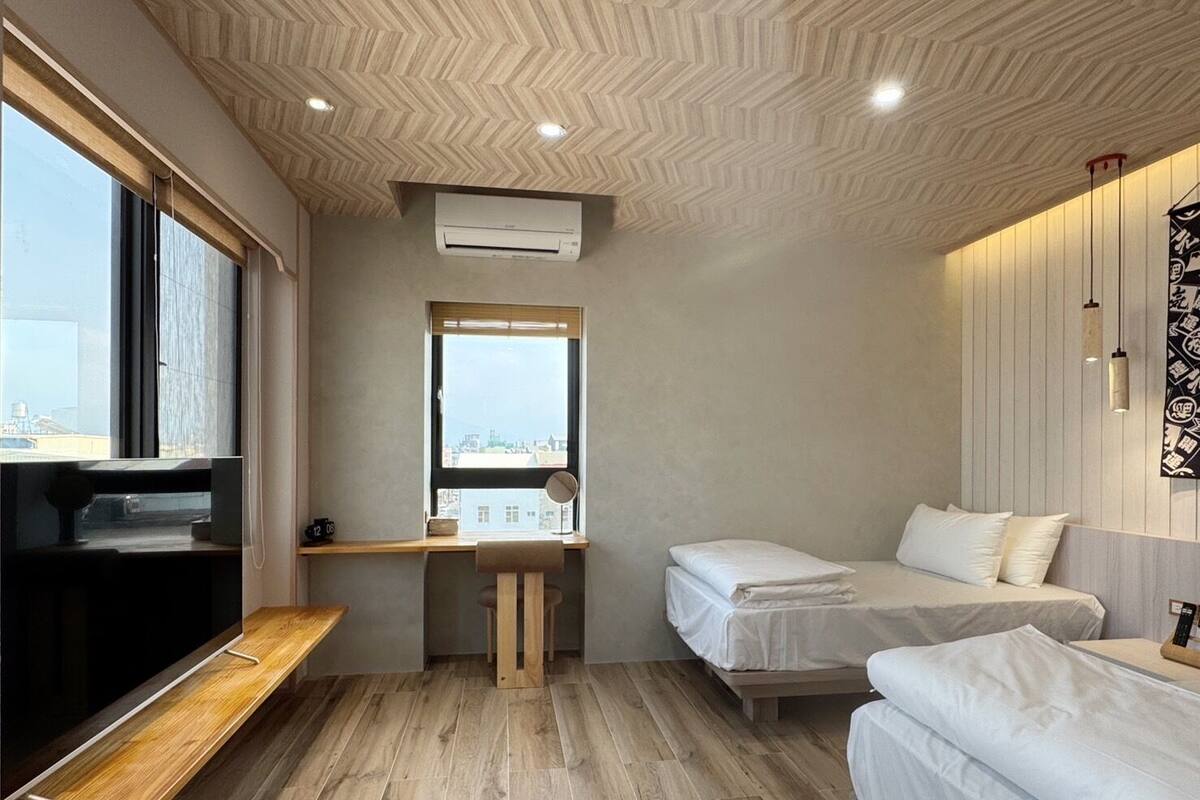 Une chambre d’hôtel compacte avec un plancher en bois, un lit, un bureau avec une chaise, une télévision et une fenêtre donnant sur la ville.