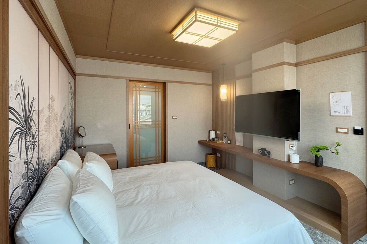 Une chambre d’hôtel avec un grand lit, un téléviseur fixé au mur, une console en bois et une porte coulissante.