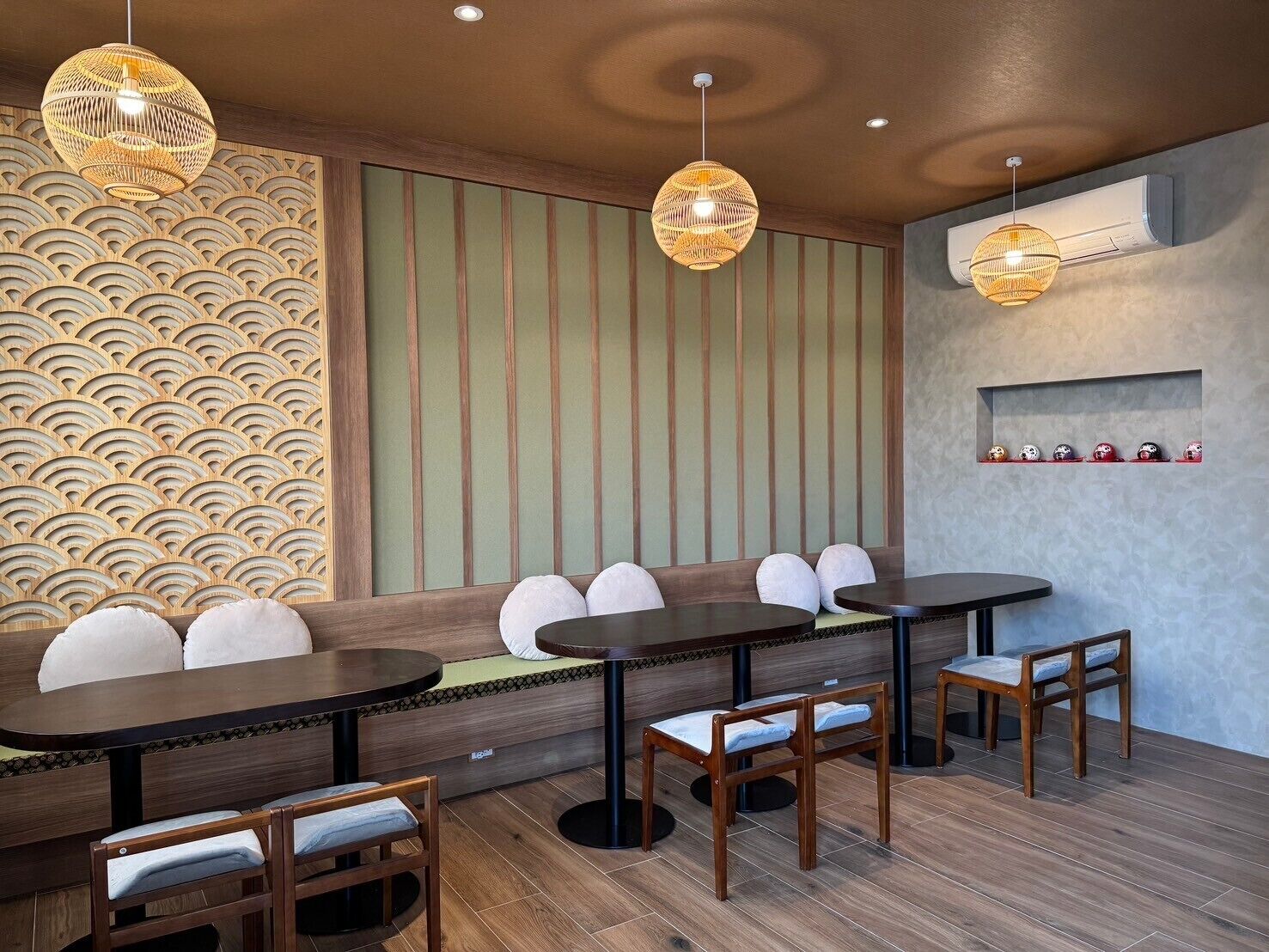 A restaurant interior with a long wooden bench, round tables, and hanging wicker lamps.