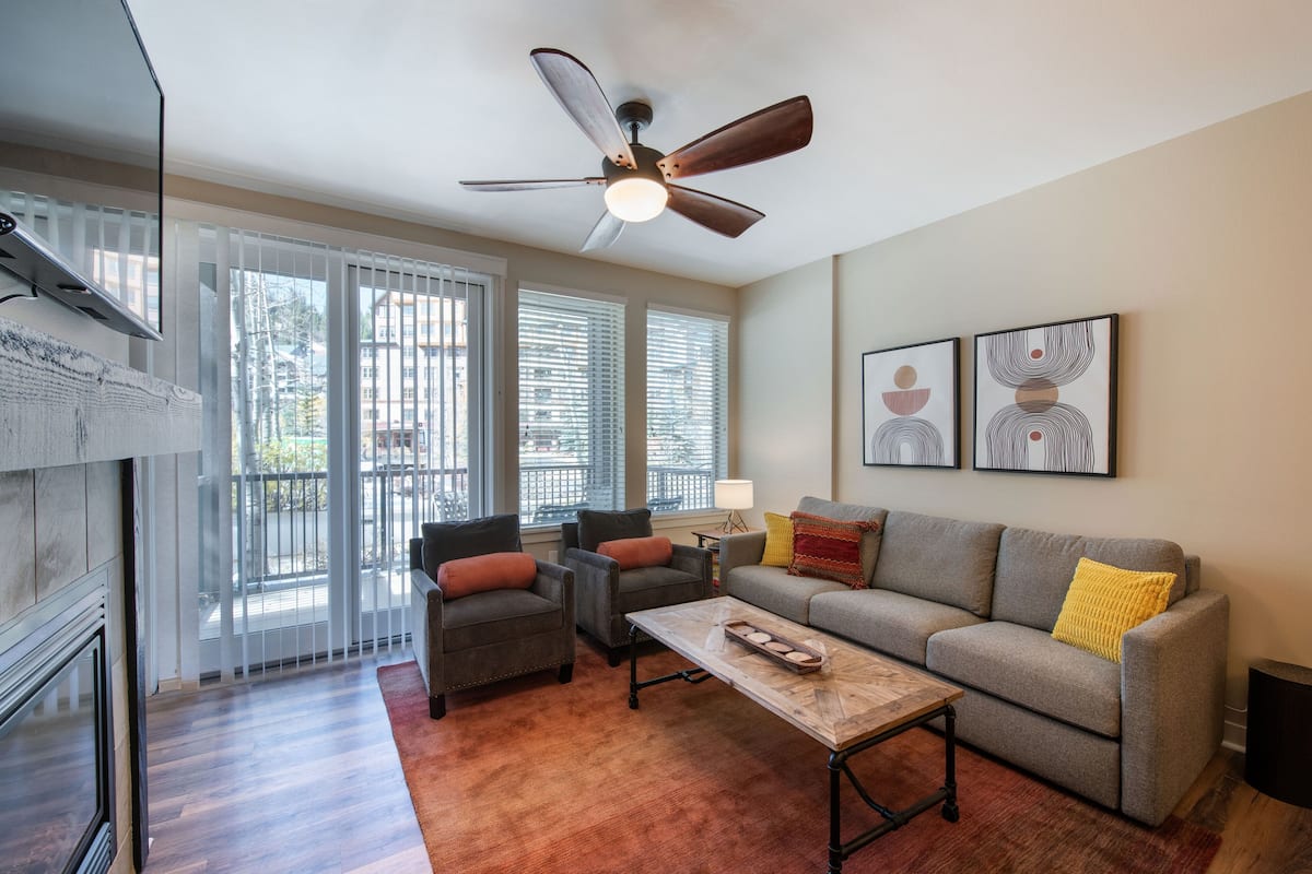 A living room with a fireplace, a ceiling fan, a sofa, two armchairs, and a coffee table.