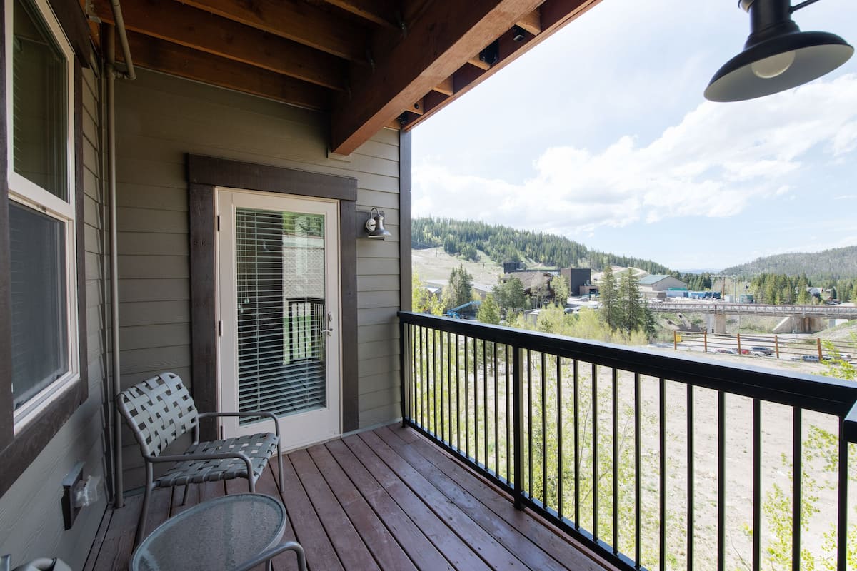 A wooden deck with a black railing, a door with a window, and a chair.