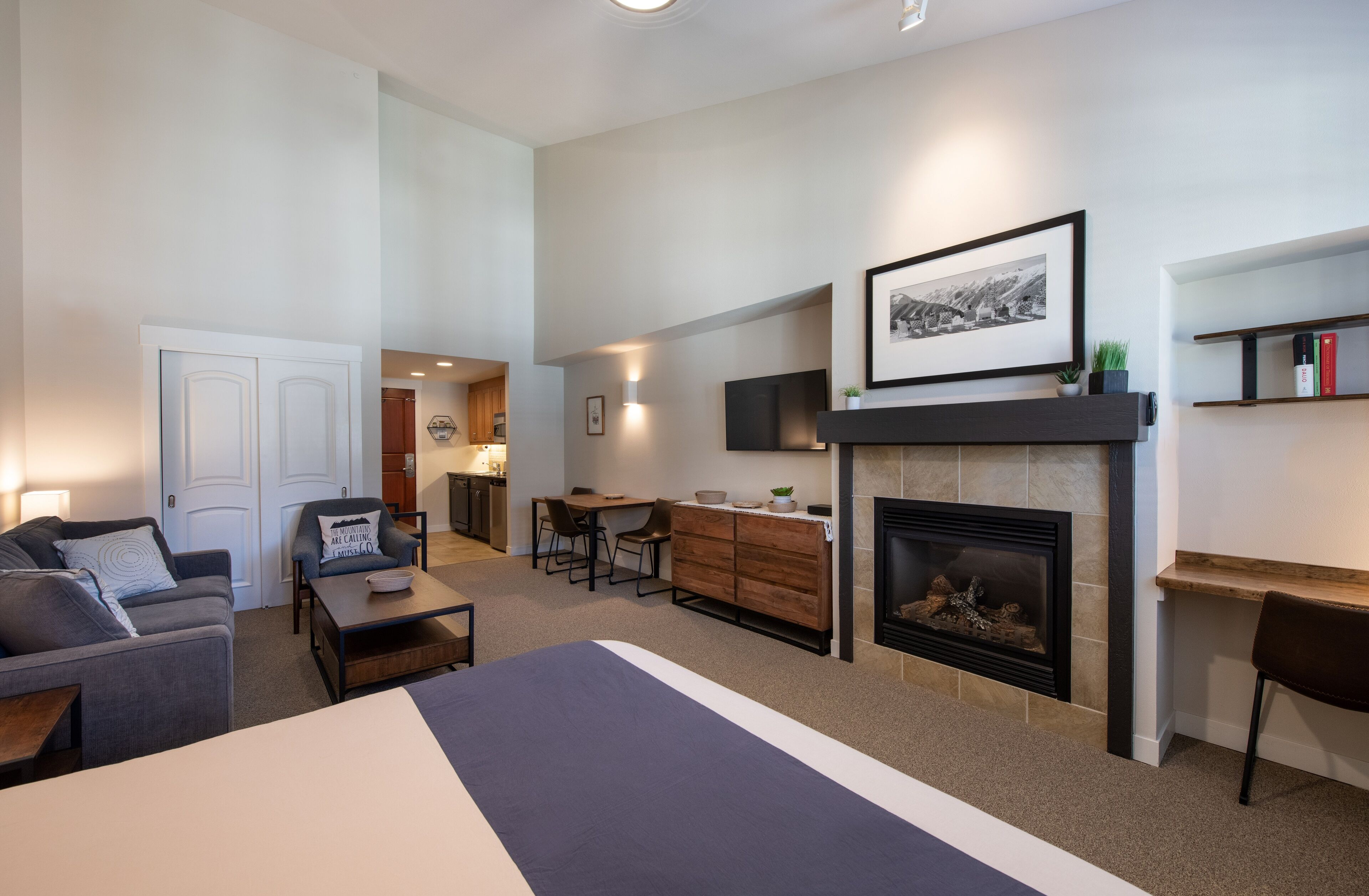 A modern living room with a fireplace, a dining area, and a kitchen visible through an open door.