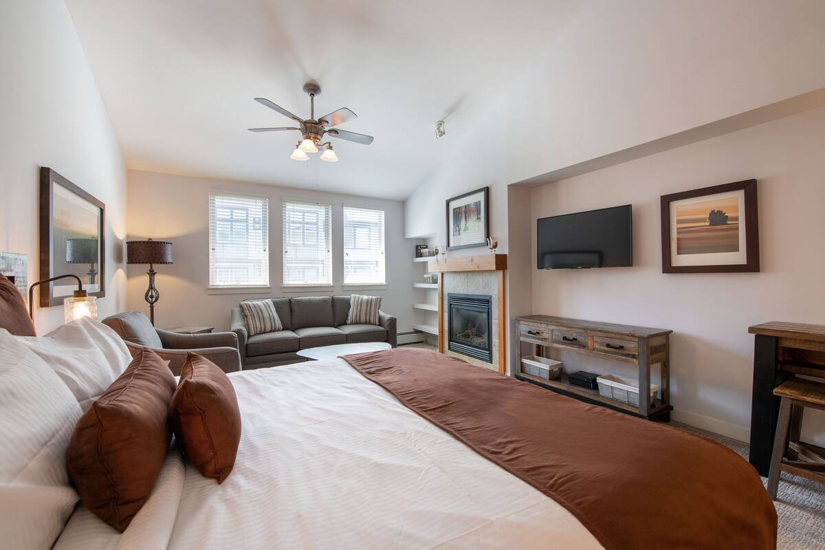 Une chambre spacieuse avec un grand lit, un canapé, une cheminée, une télévision et un ventilateur de plafond.