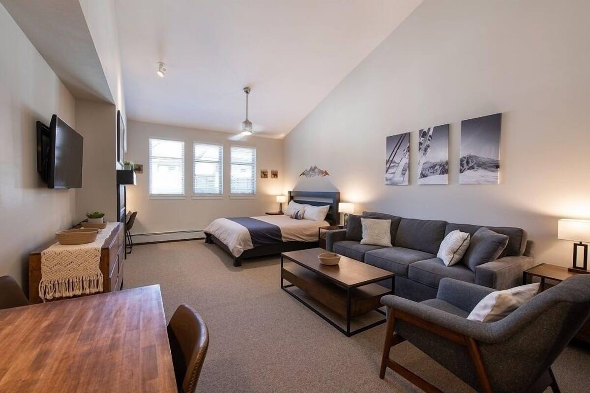 Un salon moderne avec un canapé, une table basse, un téléviseur fixé au mur et un lit doté d’une tête de lit.