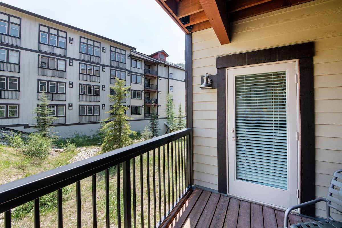 A balcony with a wooden railing, a door with a window, and a view of a multi-story building with balconies.