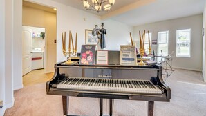 A grand piano in a spacious room with a chandelier, a framed map, and a statue. - 5 Mi to Dtwn Clermont: Family Home w/ Water Views! (Clermont)