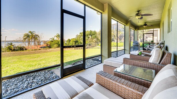 A sunlit room with large windows, wicker furniture, and a view of a grassy area and palm trees. - 5 Mi to Dtwn Clermont: Family Home w/ Water Views! (Clermont)