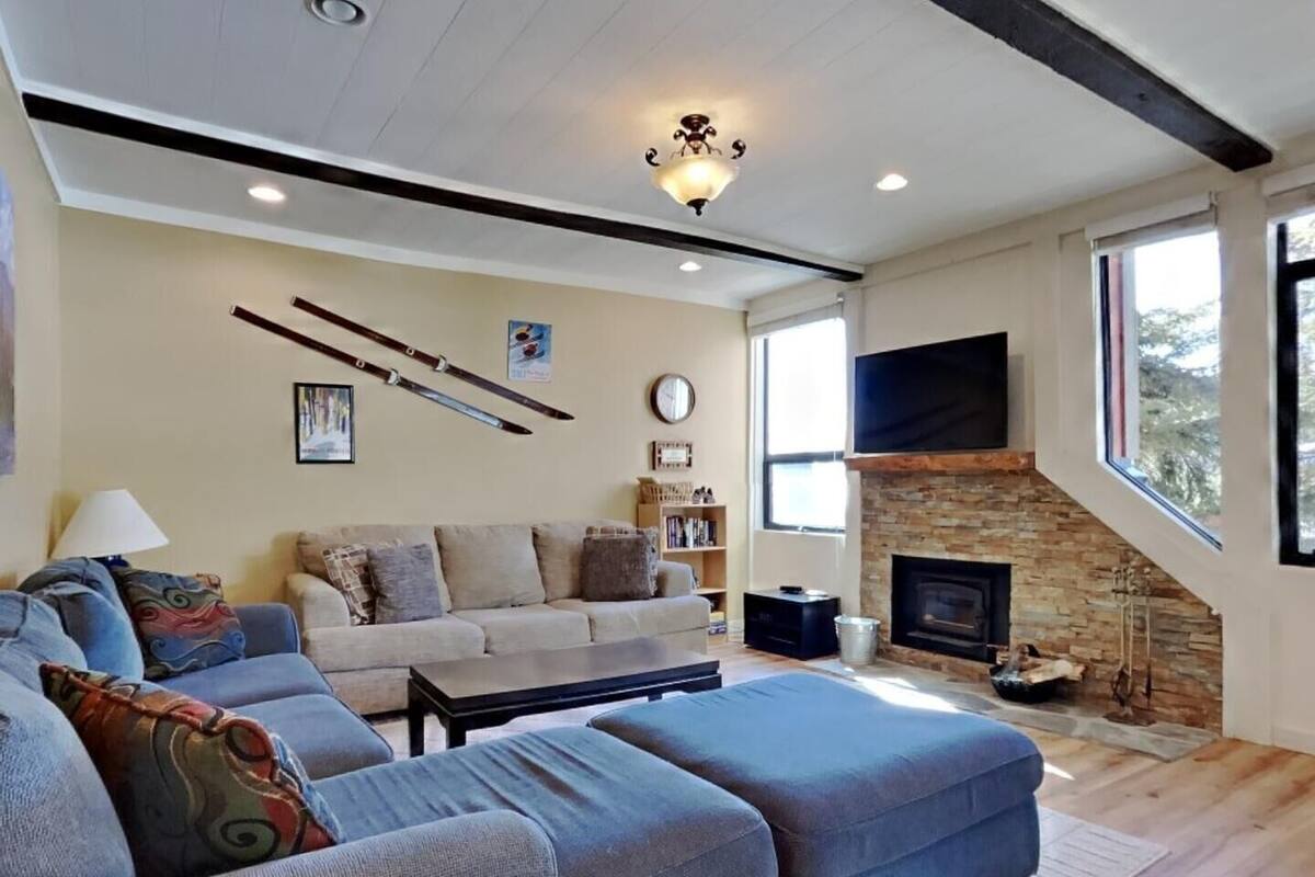 A living room with a sectional sofa, a fireplace, a flat-screen TV, and a stone wall.