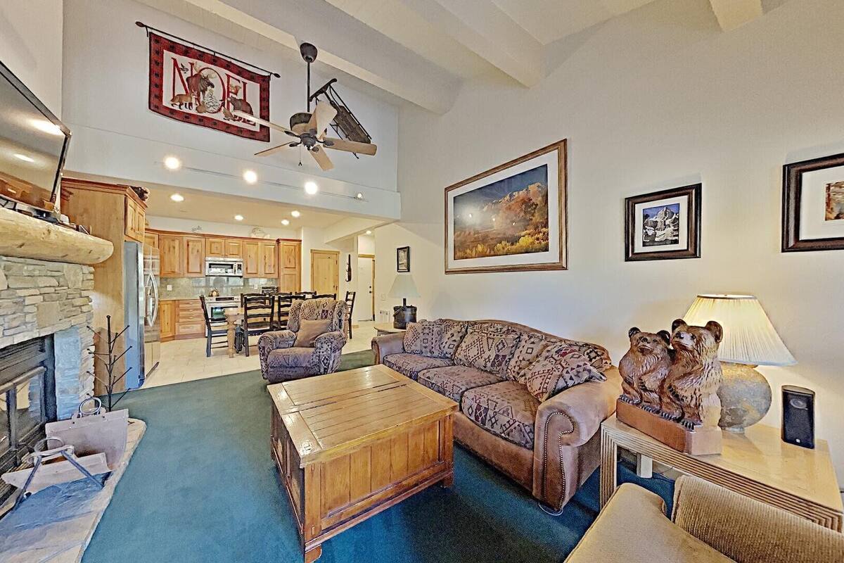 A spacious living area with a stone fireplace, a wooden coffee table, a patterned sofa, and a dining area in the background.