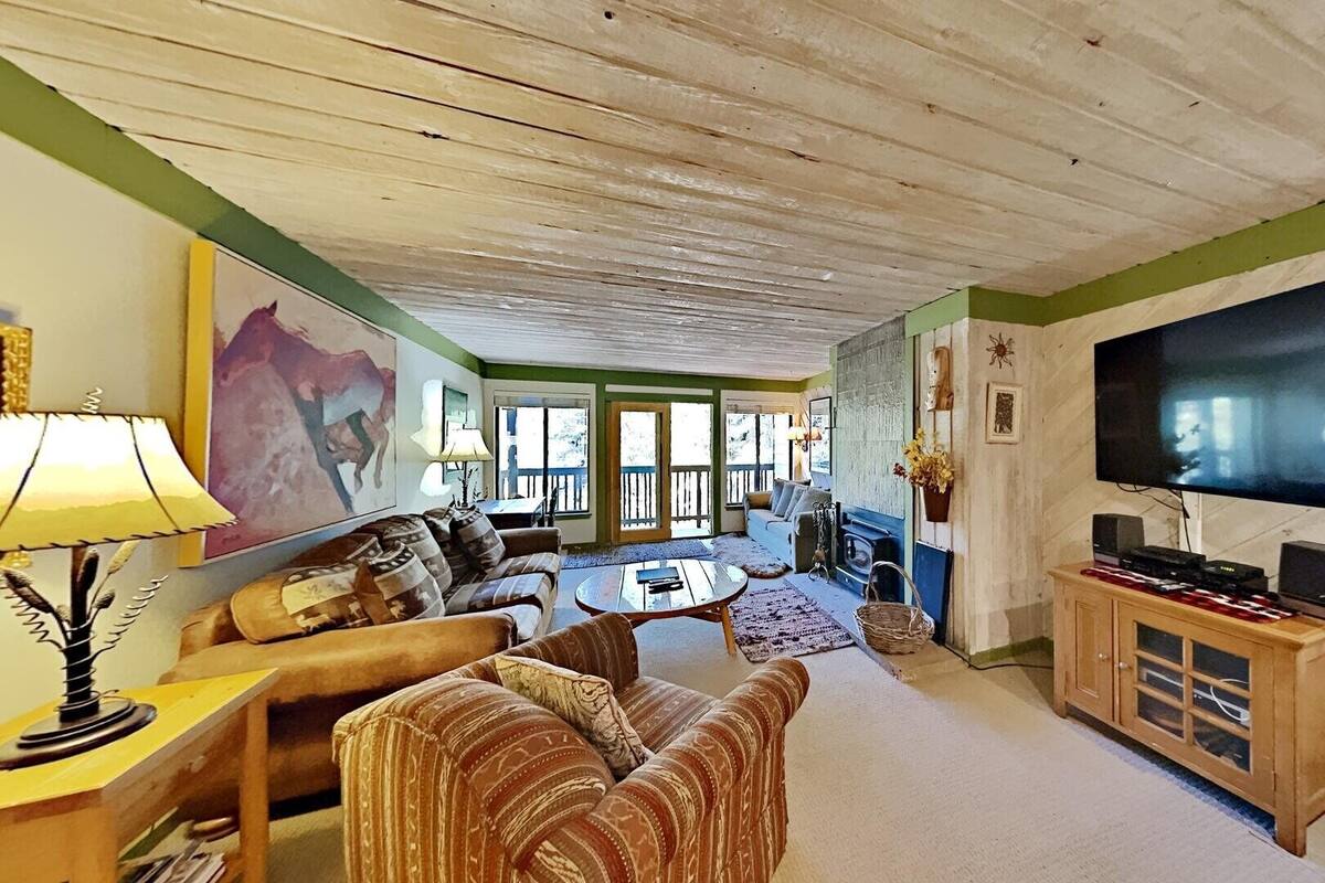 A cozy living room with a large TV, comfortable seating, and a view of the outdoors.