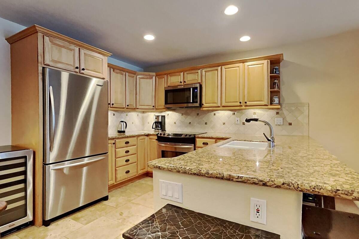 A modern kitchen with stainless steel appliances, wooden cabinets, granite countertops, and a built-in oven.