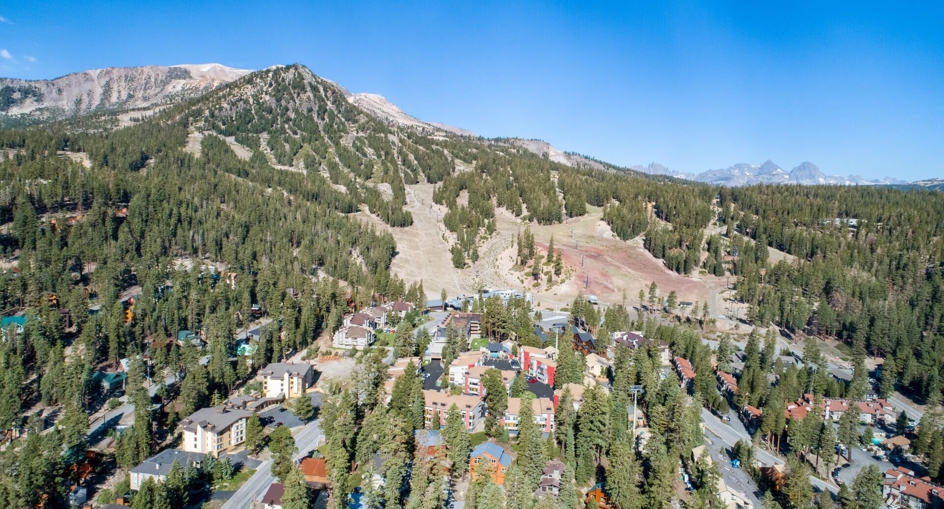 Un quartier résidentiel où les maisons sont entourées de forêts denses et où l’on aperçoit des montagnes au loin.