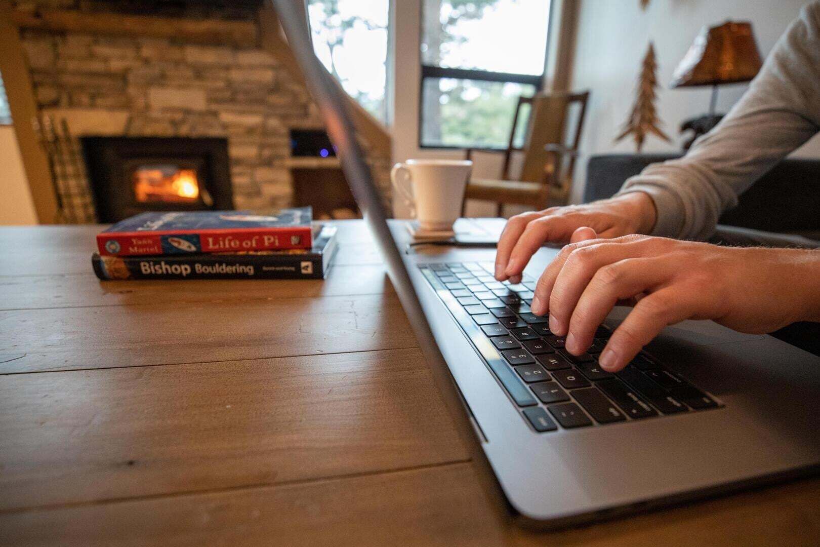 A laptop on a wooden table with books and a cup.