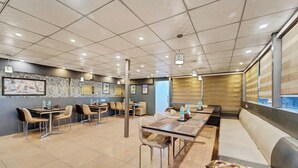Ein modernes Restaurant mit einem langen Gemeinschaftstisch, separaten Sitzecken und einer Sitzgruppe mit gepolsterten Bänken.