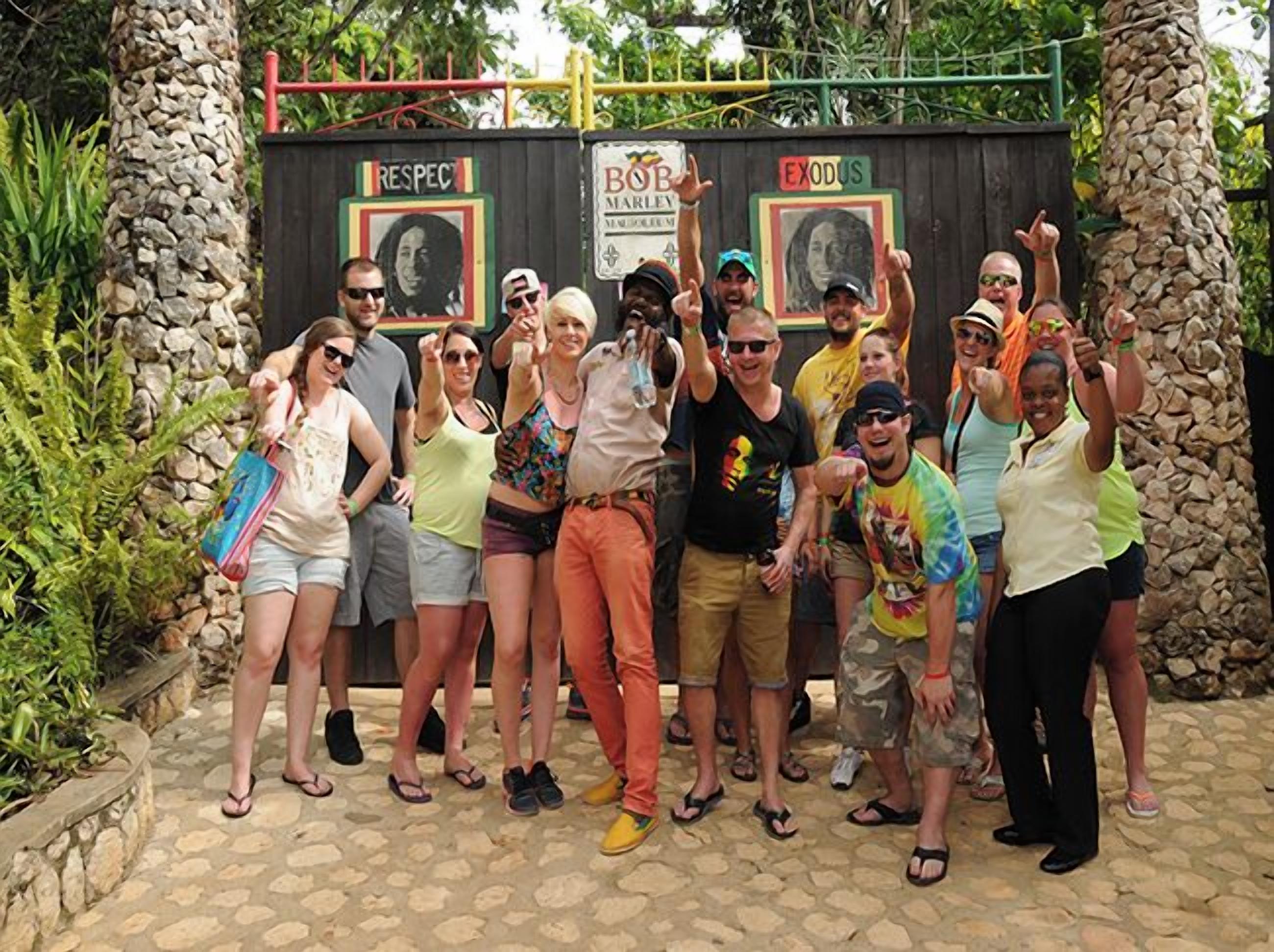 Een groep mensen poseert voor een houten constructie met twee borden, waarvan er één een portret en de woorden 'RESPECT' en 'EXODUS' heeft, en de ander een portret en de woorden 'BOB MARLEY'.