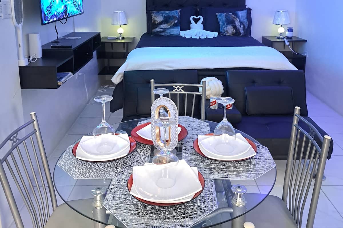 Una camera d'hotel con un letto, una TV, un tavolo da pranzo apparecchiato per due persone e una ventola a soffitto.
