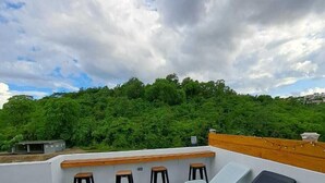 A rooftop patio with stone flooring, a wooden bench, and lounge chairs.
