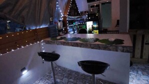 A bar area with two stools, a stone-tiled floor, and string lights.