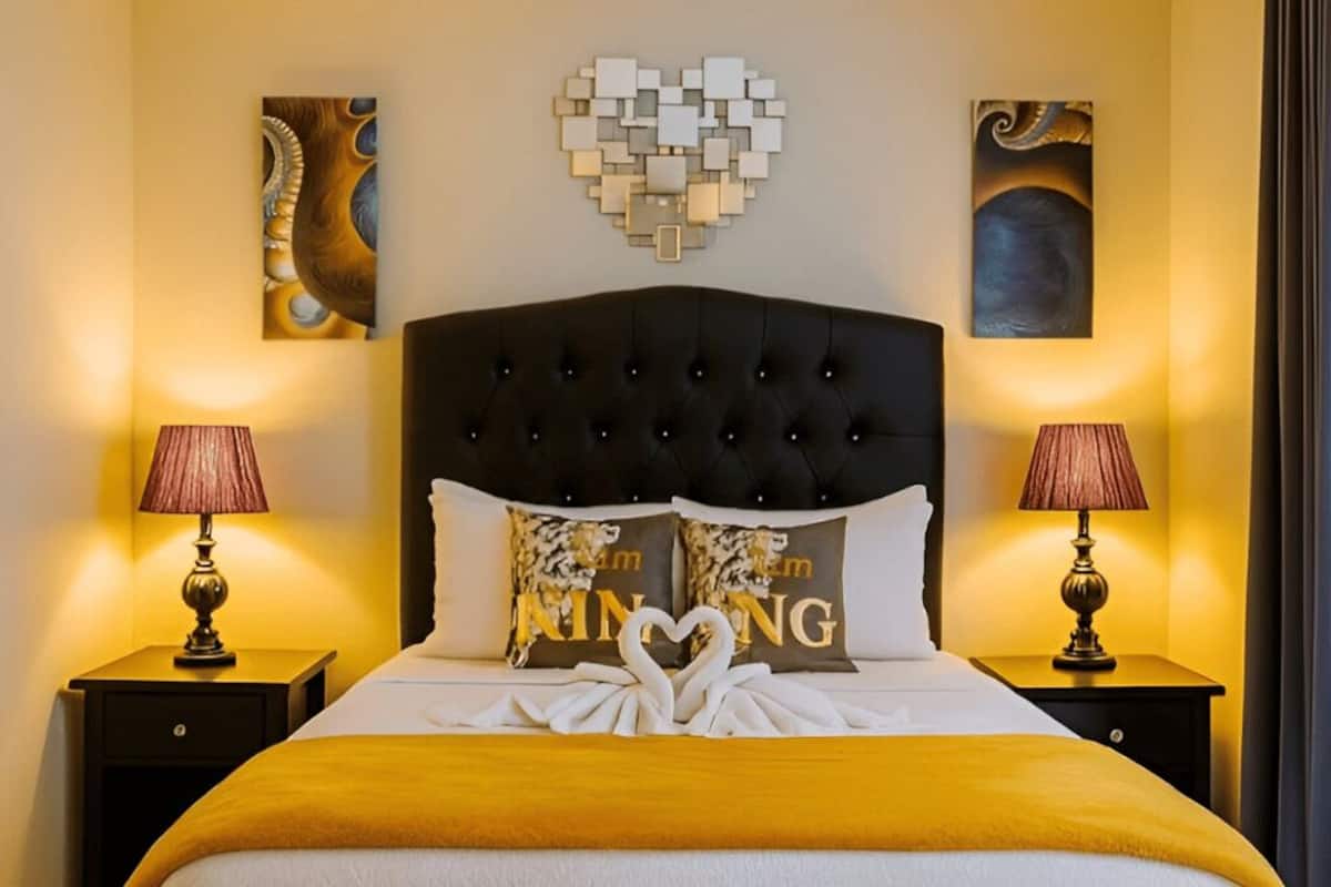 Una camera d'albergo con testiera trapuntata, due abat-jour, un letto con una coperta dorata e cuscini decorativi.