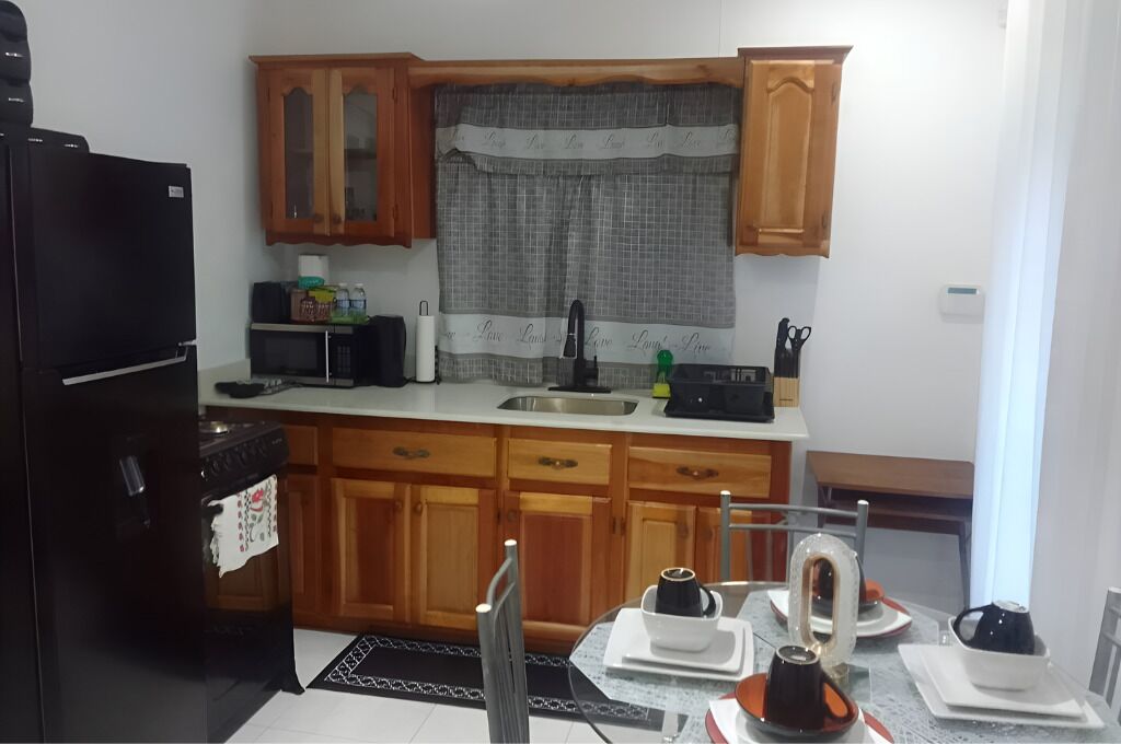 A compact kitchen with wooden cabinets, a black refrigerator, a microwave, and a dining table set with plates and cups.