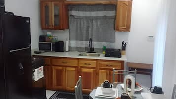 A compact kitchen with wooden cabinets, a black refrigerator, a microwave, and a dining table set with plates and cups.