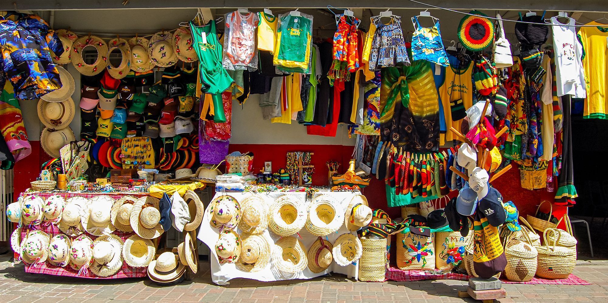 Un étal de marché proposant divers chapeaux, sacs et vêtements aux couleurs vives.