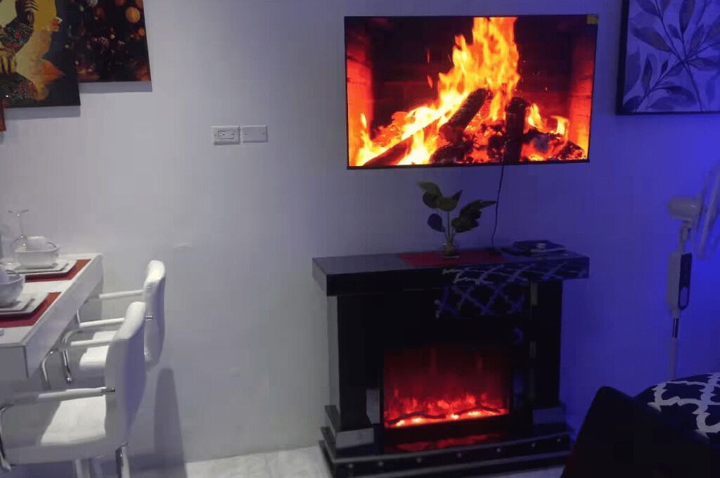 Una sala de estar con chimenea, una mesa de comedor con sillas y un televisor colocado sobre la chimenea mostrando un fuego.