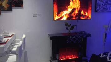 Una sala de estar con chimenea, una mesa de comedor con sillas y un televisor colocado sobre la chimenea mostrando un fuego.